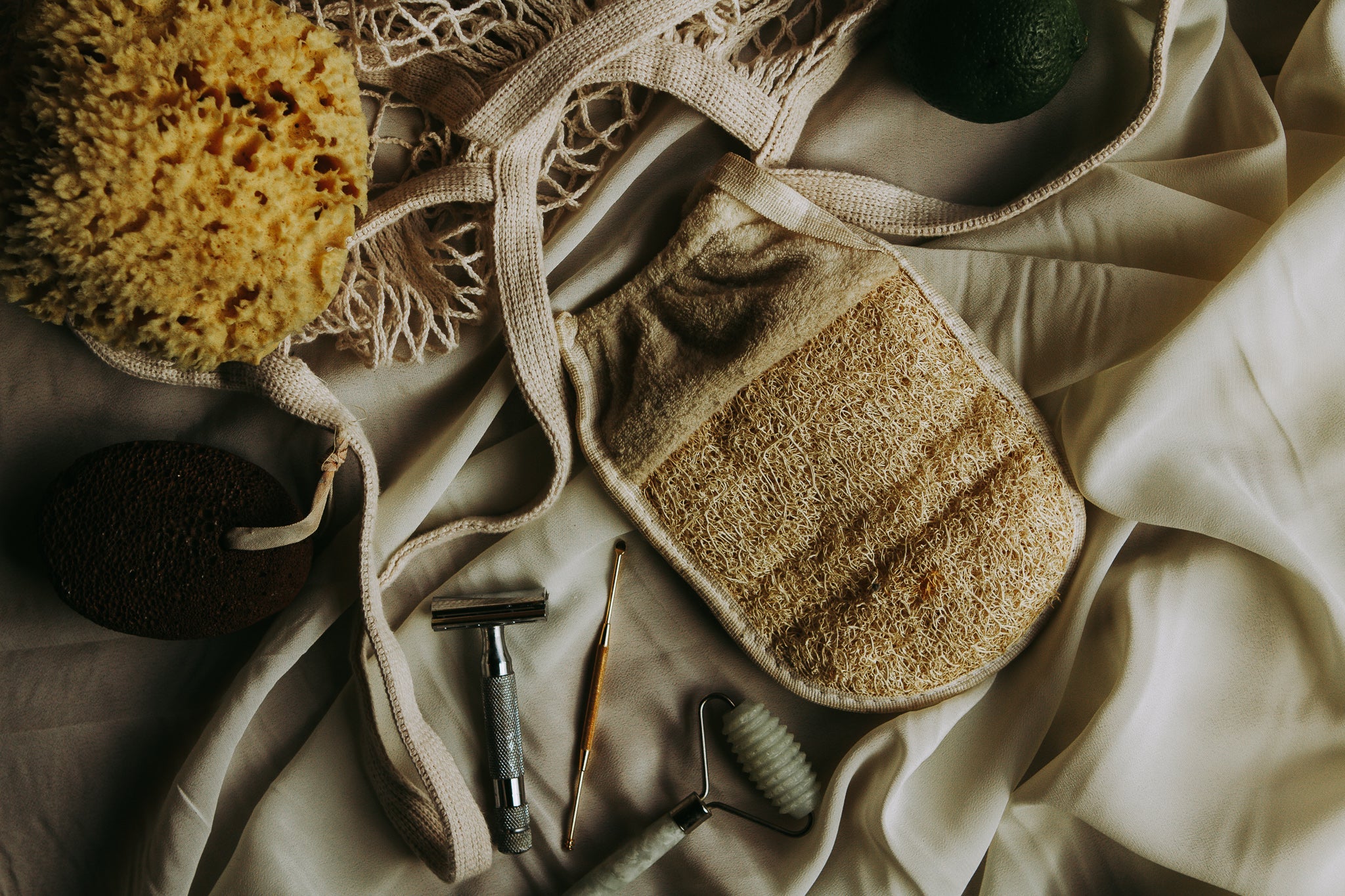 Reusable cleaning products, safety razor, sea sponge, and organic body scrubber on a light fabric background