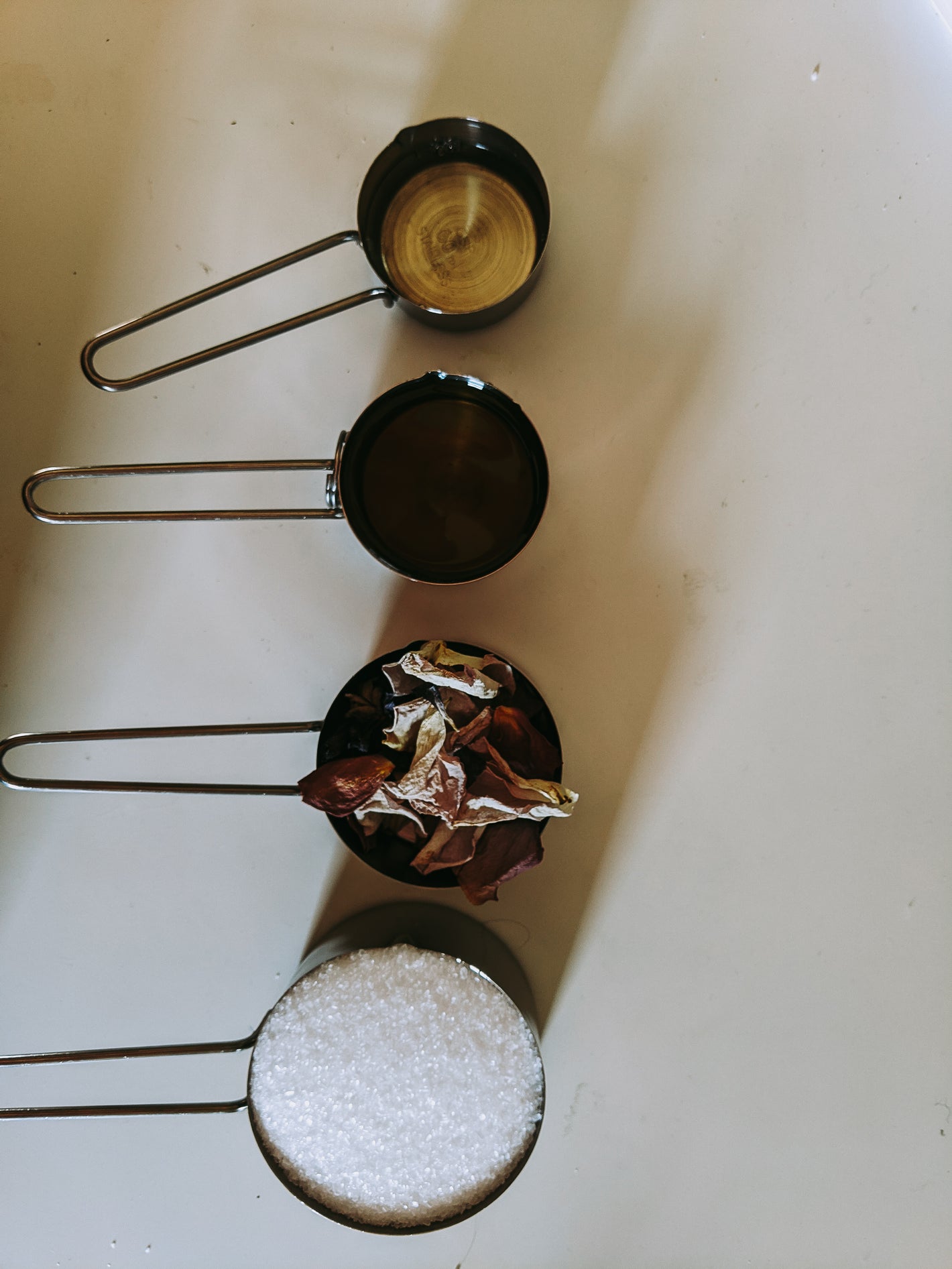 Four dry measuring cups with salt, oil, fragrance, and dried rose petals