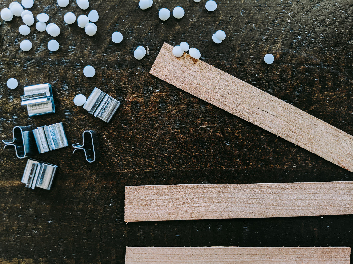 flat wooden wicks, wick clips, and soy wax beads lay on a wooden table