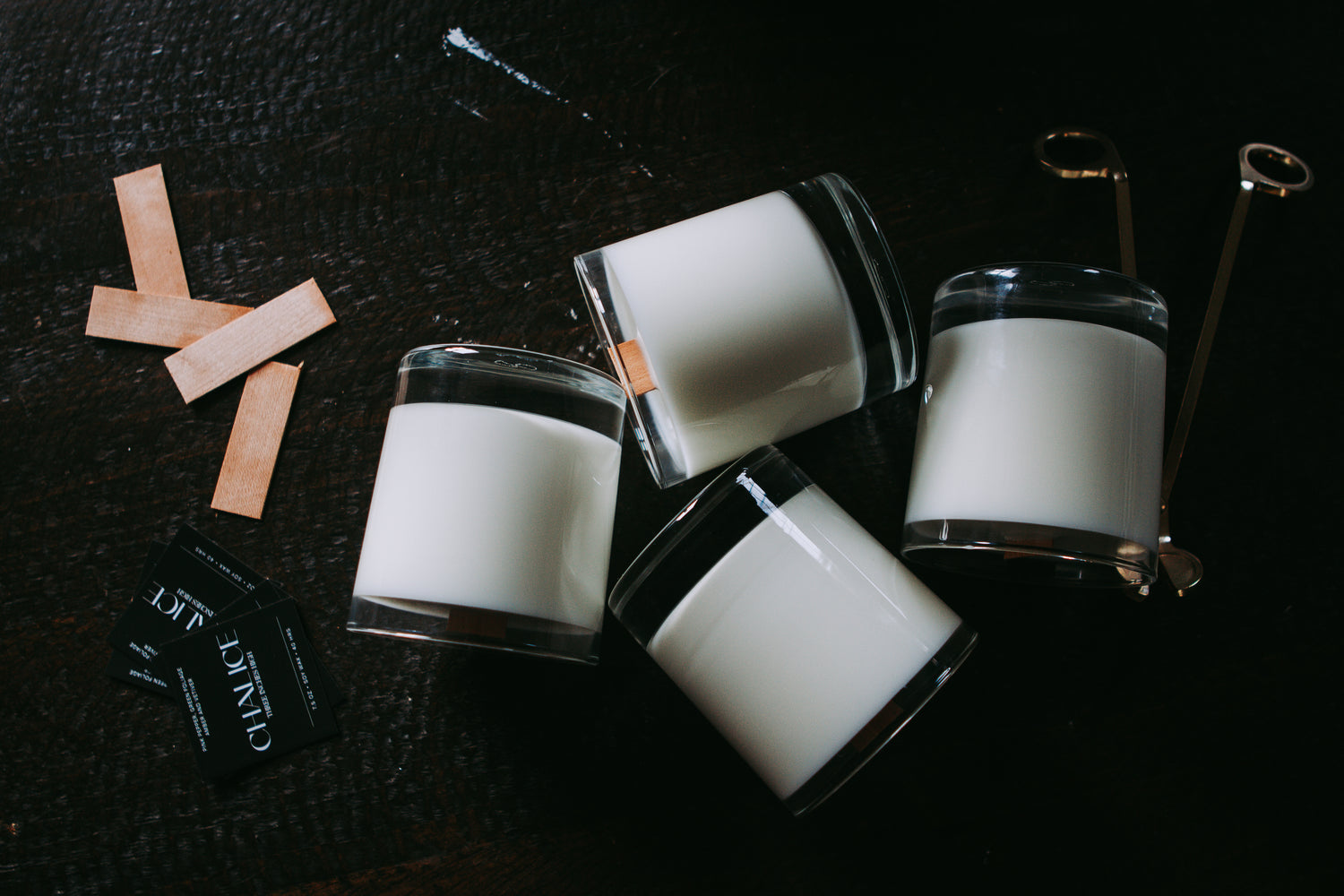 soy wax candles and flat wooden wicks lay on a dark wooden table