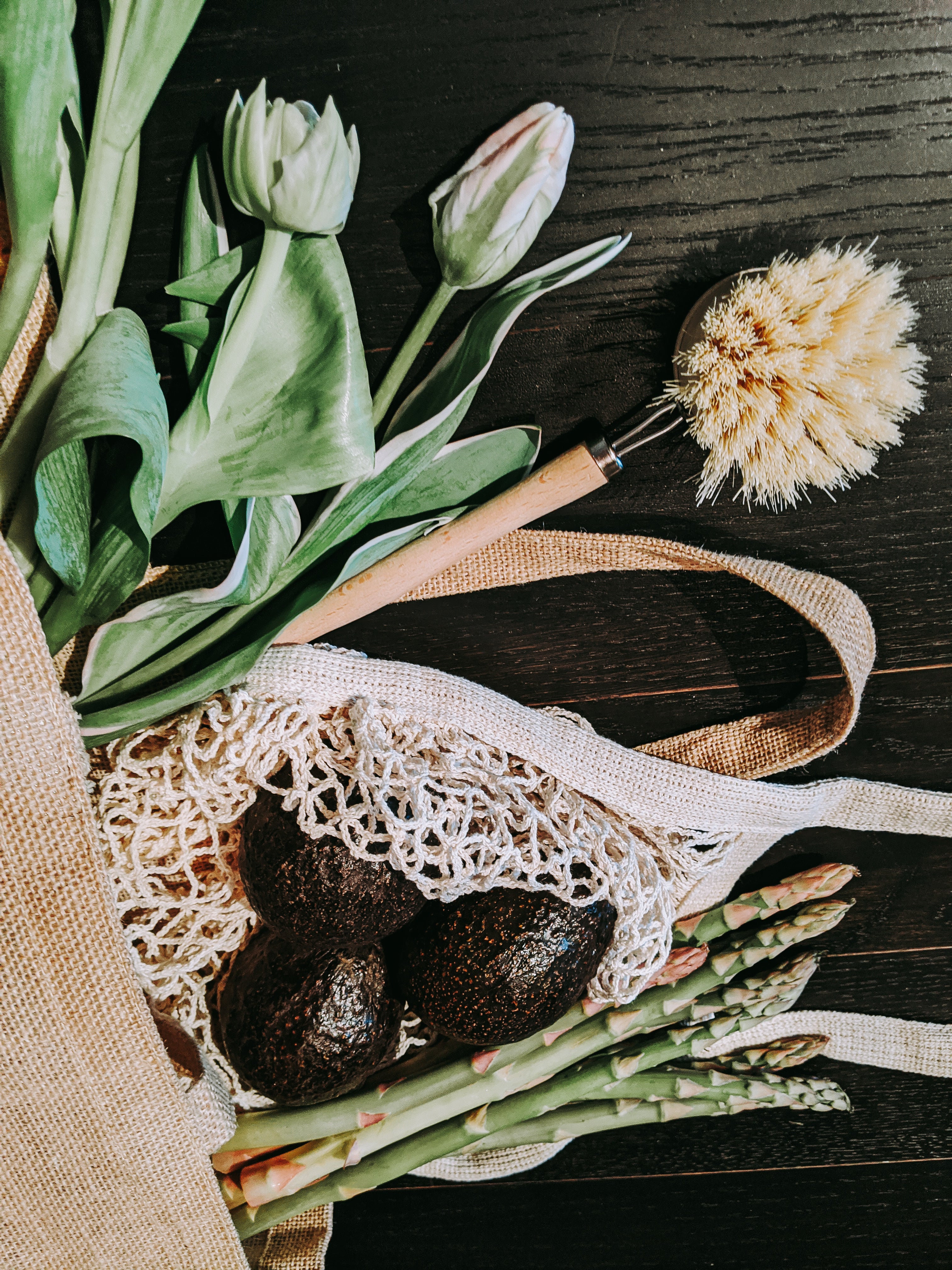 green tulips, asparagus, and avocados spill out of a reusable shopping bag