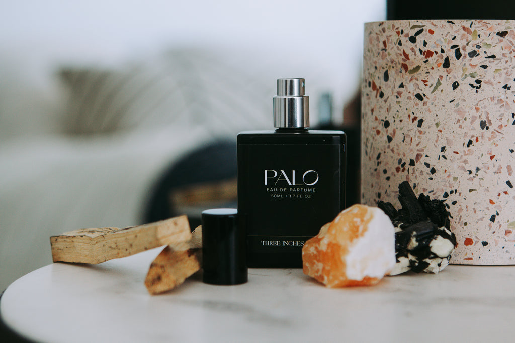 A black bottle of 'Palo' eau de parfume with a spray dispenser, displayed next to its cap on a wooden surface.